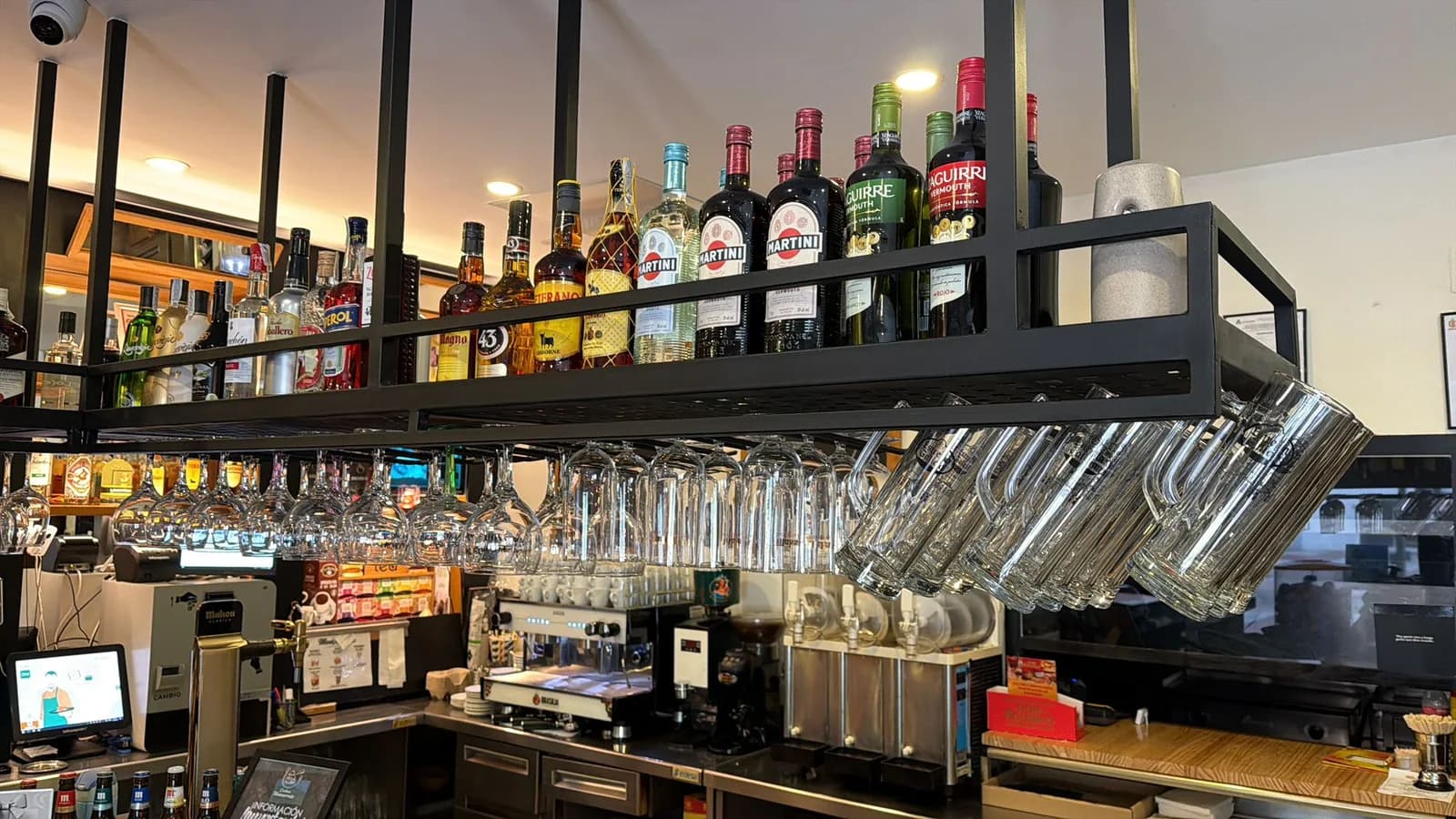 Botellero suspendido sobre la barra con vermuts, licores y copas colgadas